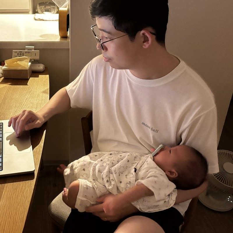 Guang Li working at home while holding his baby